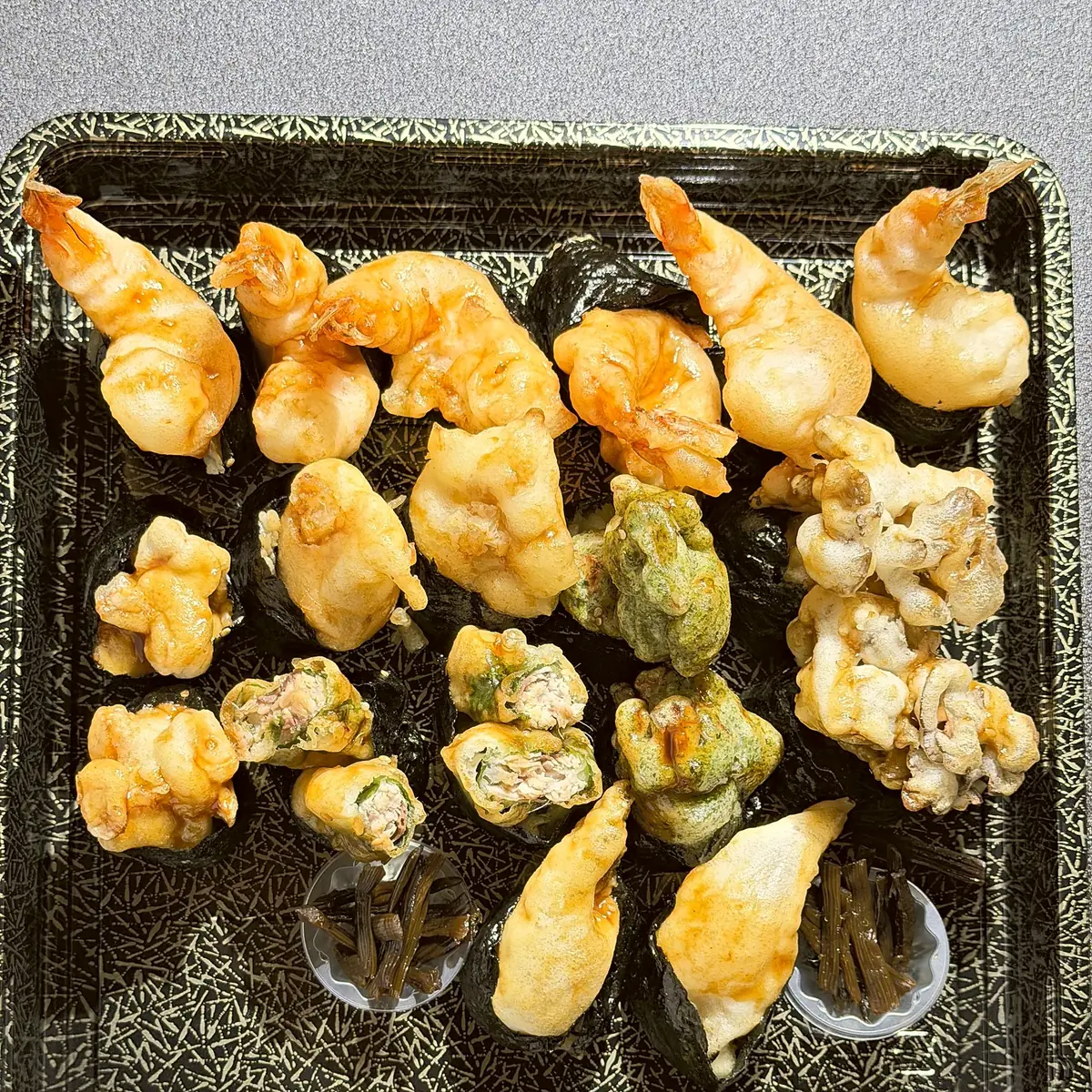 黒い盛り台に並んだ天むす18貫。尾の付いた大海老天むすと、季節の天むす