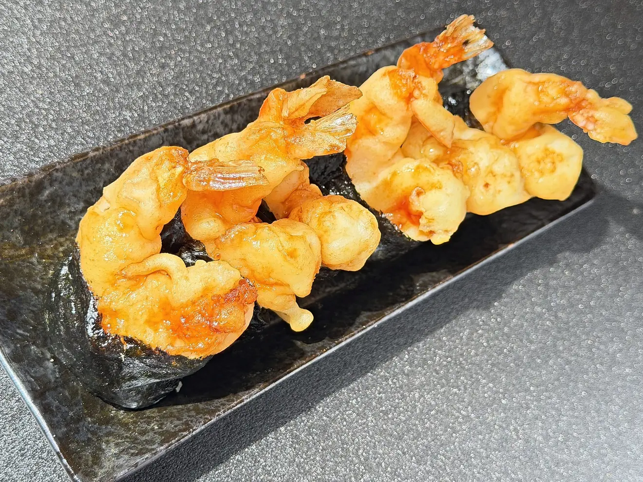 黒い角皿に並んだ大海老天むす。タレをからめた大海老の天ぷらが、尾まで見える